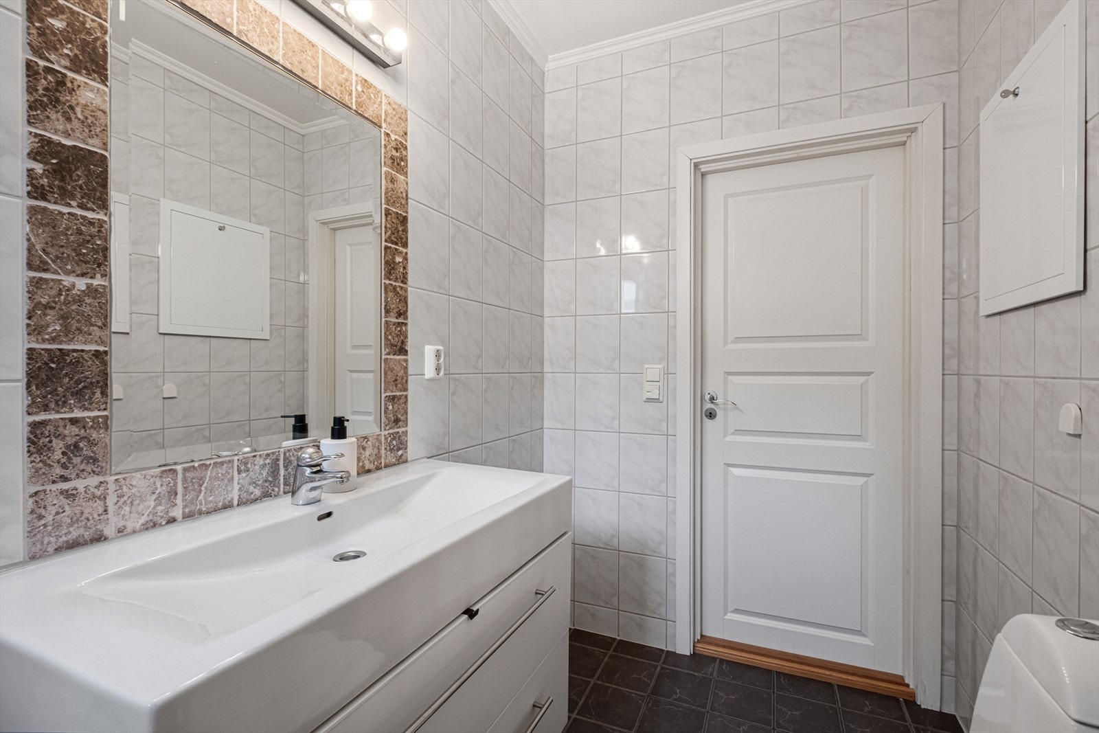 Badet har innredning med nedfelt servant, toalett, dusjvegger/hjørne og opplegg for vaskemaskin. Galleribilde