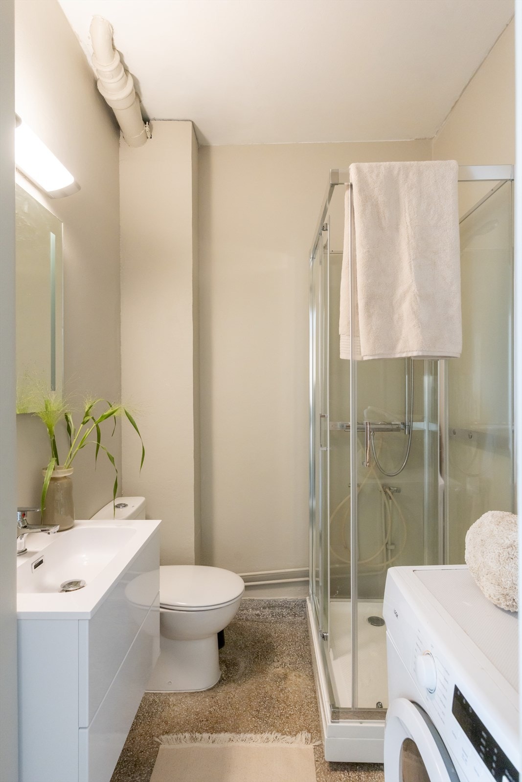 Badet har slipt betonggulv, malte veggflater, dusjkabinett, gulvmontert toalett og servant. Galleribilde