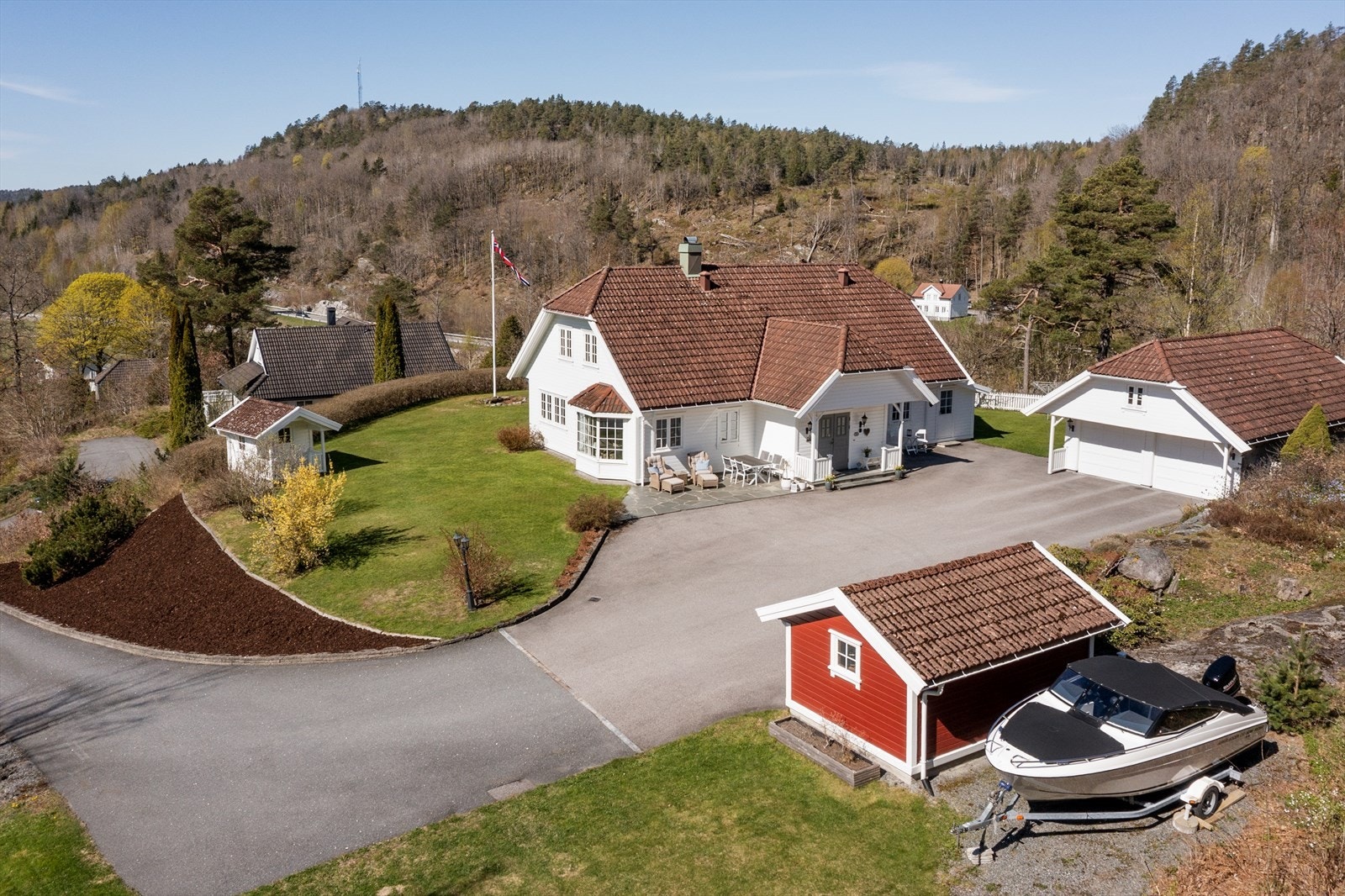 Dronefoto. Hage og tomt er særdeles velstelt med asfaltert adkomst/tun, plen, skiferplatting, bed og variert beplantning. Galleribilde