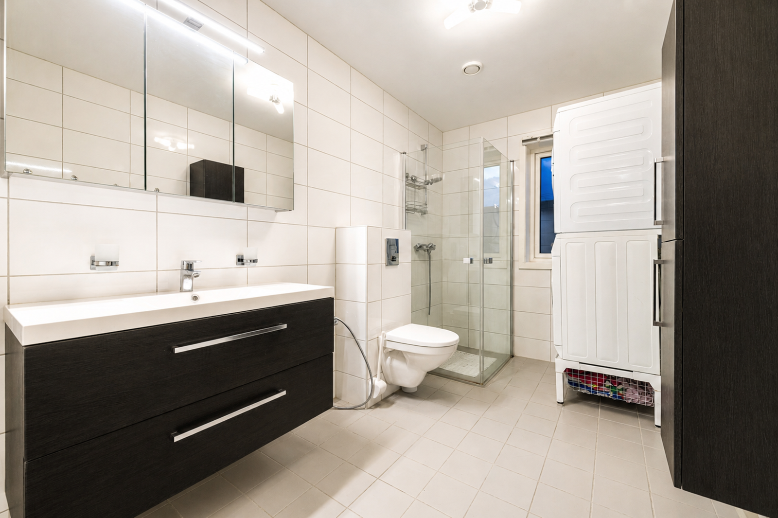 Badet i 1. etasje er flislagt og utstyrt med varmekabler, dusjdører, vegghengt toalett, baderomsinnredning og opplegg for vaskemaskin Galleribilde