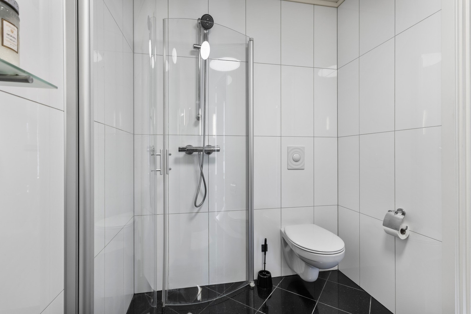 Badet har dusjhjørne, vegghengt toalett og lyse flislagte vegger. Galleribilde
