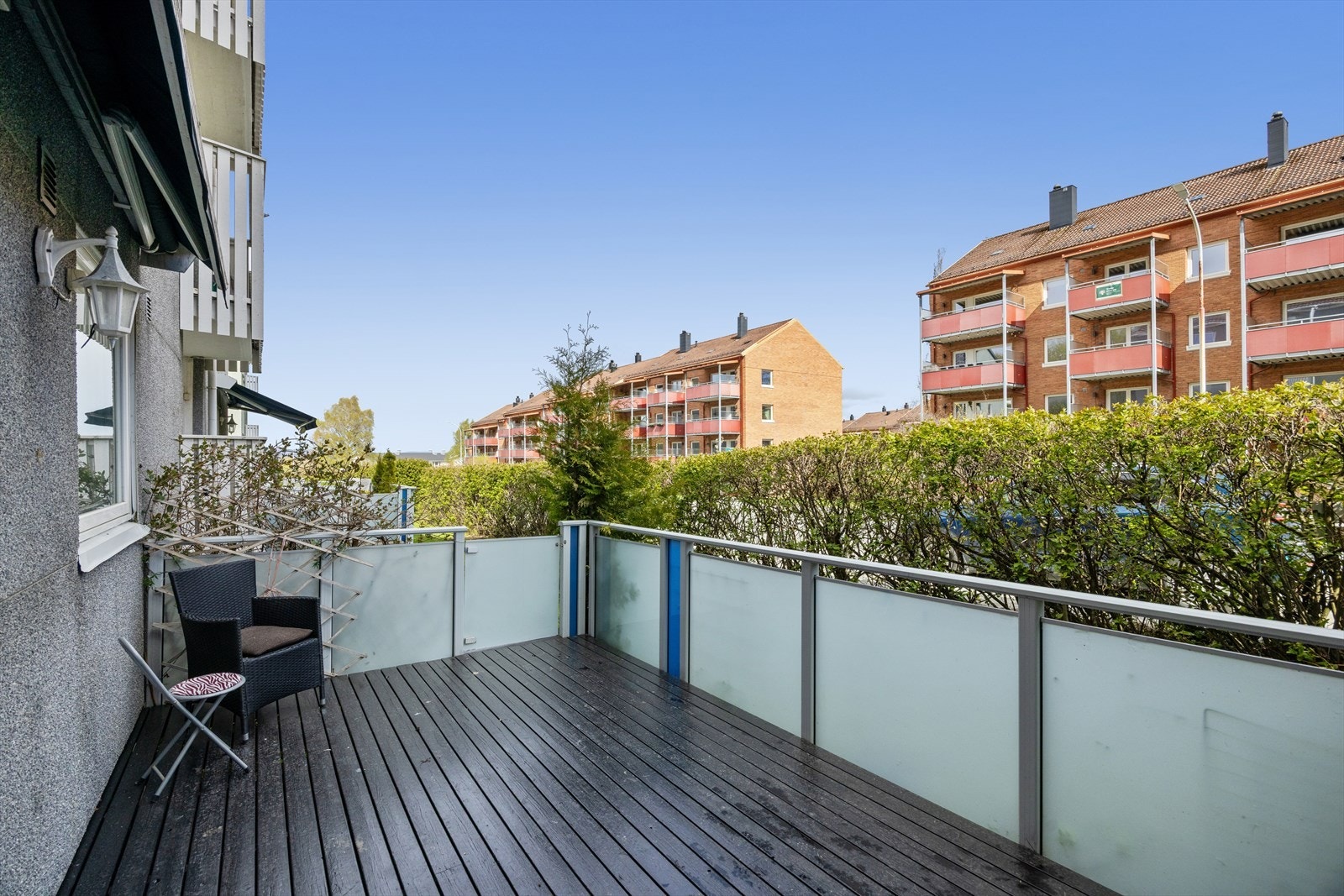 Lun og usjenert veranda som er skjermet fra gaten med en grønn og frodig hekk på sommerstid. Galleribilde