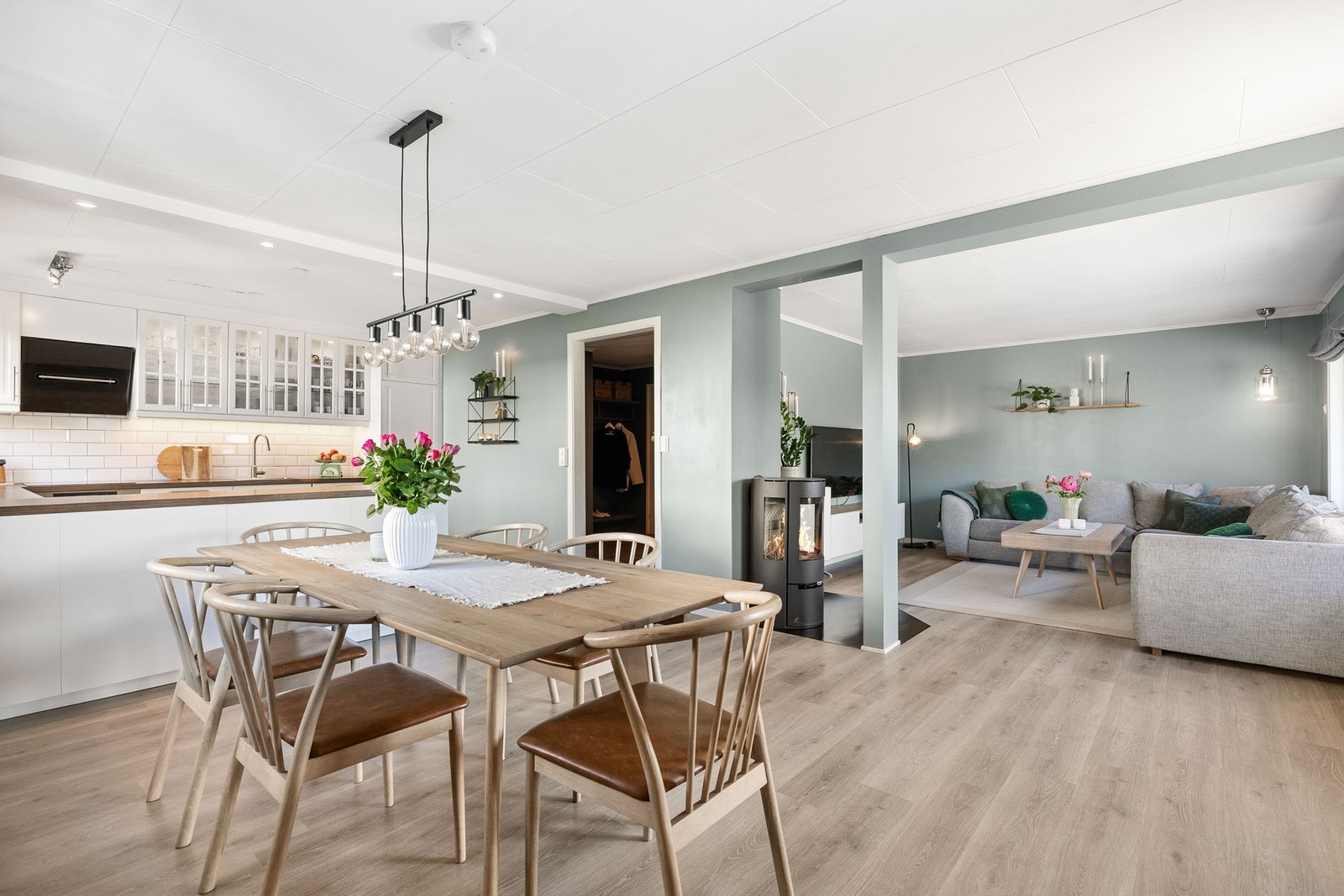 Det er åpen løsning mellom kjøkken og stue, med peis som gir en hyggelig atmosfære. Lyse farger og store vinduer bidrar til et godt førsteinntrykk! Galleribilde