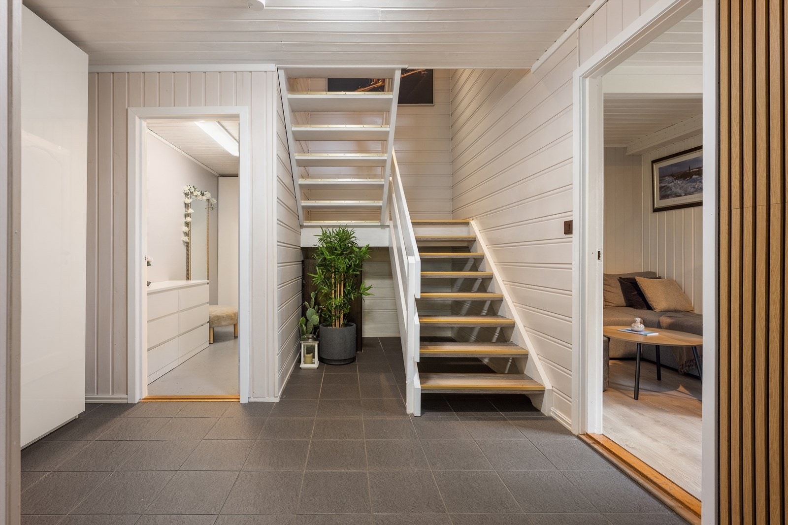 Gangen har flislagt gulv, skyvedørsgarderobe for oppbevaring og trapp opp til hovedetasjen. Galleribilde