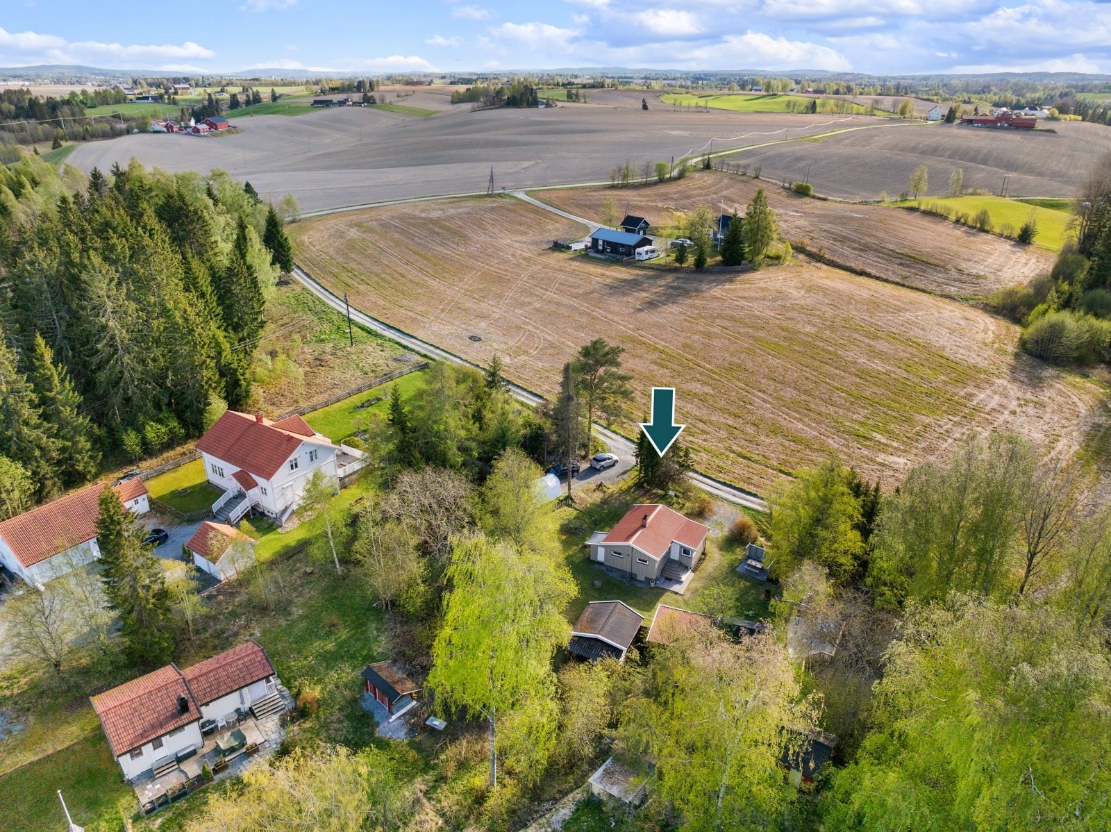 Eiendommen sett fra luften, omkranset av frodig vegetasjon og åpne jorder. Galleribilde