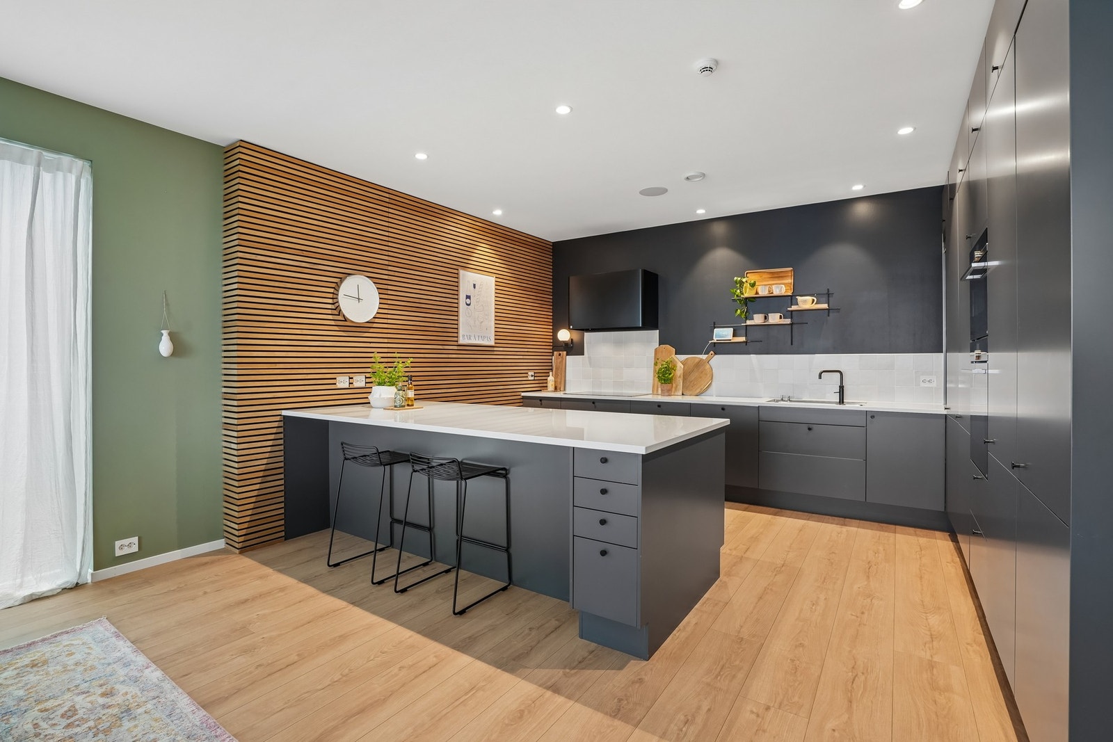 Funksjonelt, påkostet og innholdsrikt kjøkken fra Sigdal med mørke glatte takhøye fronter og fliser på vegg over Silestone benkeplate. Galleribilde
