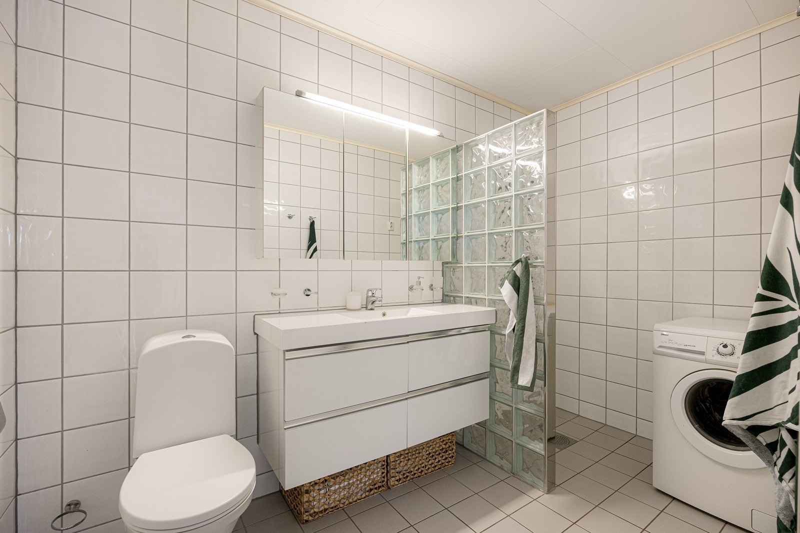 Badet er utstyrt med en heldekkende servant med skuffeseksjon, frittstående toalett, dusjnisje med vegg av glassbyggerstein og dusjgarnityr. Det er opplegg for vaskemaskin. Galleribilde