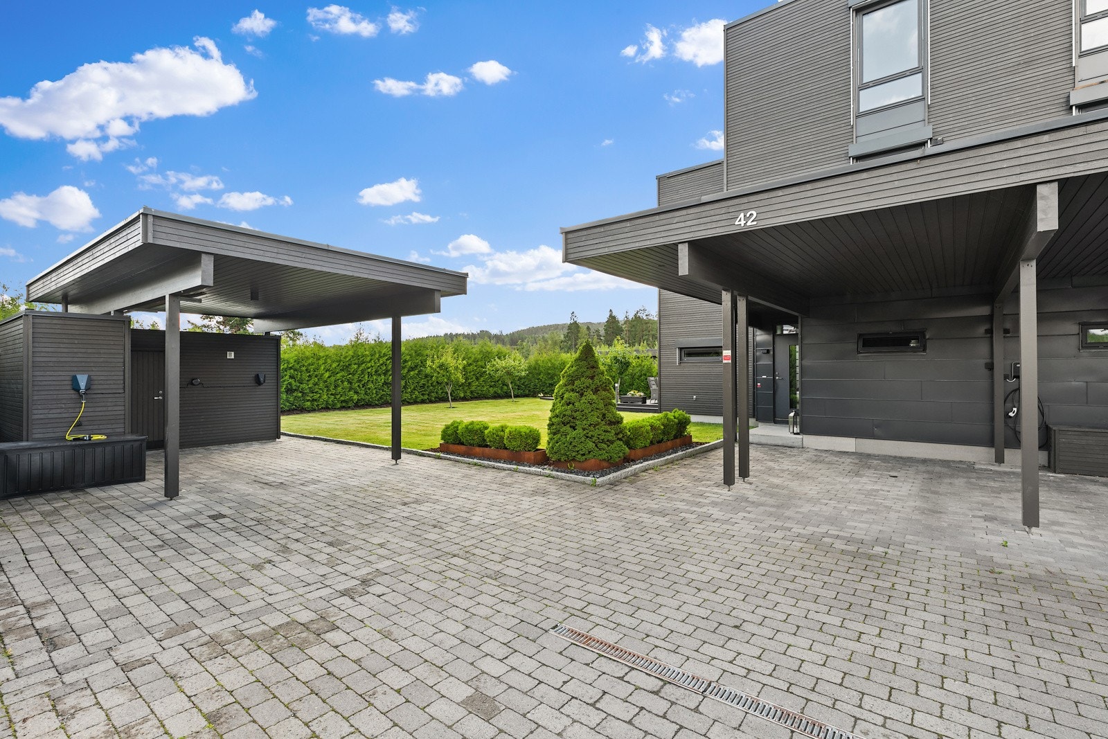 Romslig steinlagt gårdsplass med carport, opplegg for el-billader og egen utebod. Galleribilde