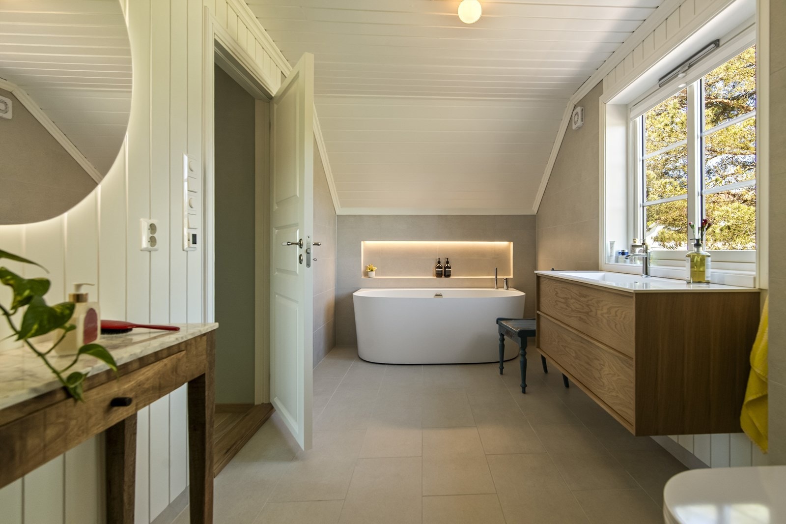 Varme er lagt i gulvet, og badet har vegghengt toalett og et elegant badekar. Ved badekaret er det en innebygd nisje med lyslist, og på motsatt side er det oppbevaring i en større nisje langs kneveggen. Galleribilde