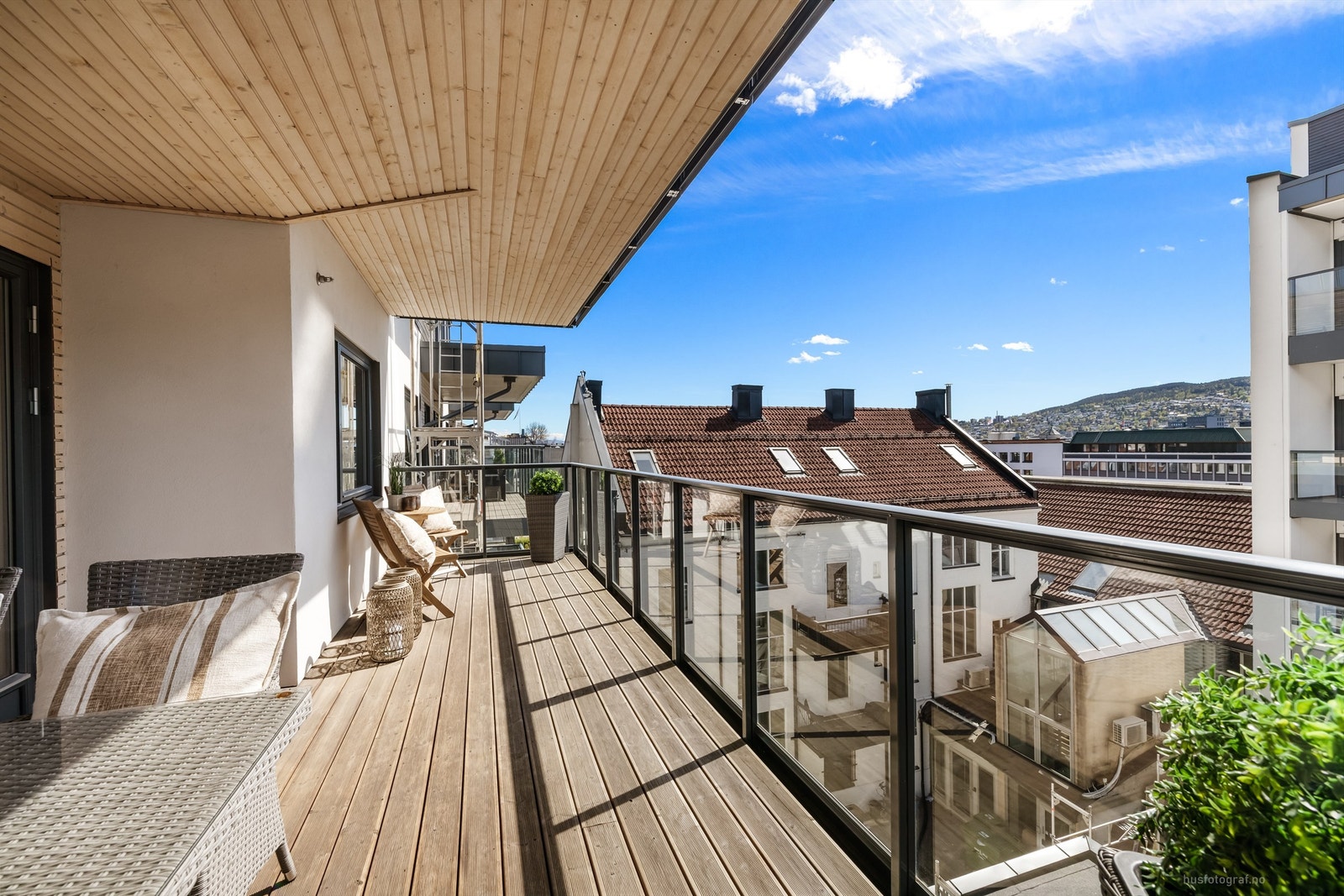 Balkongen er i betongkonstruksjon med rekkverk av metall og glass, og terrassebord på gulvet. Galleribilde