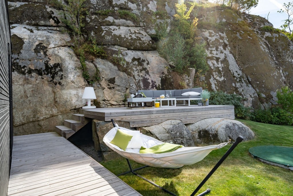 Tomten er opparbeidet med plen og terrasser som er naturlig integrert i det skrånende terrenget og fjellknausene. Galleribilde