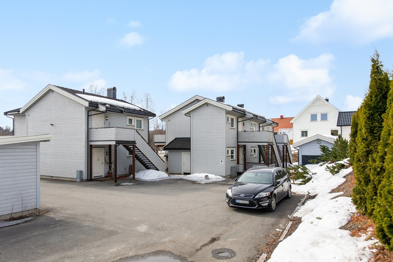 Asfaltert gårdstun med parkeringsplasser, carport i rekke og boder. Galleribilde