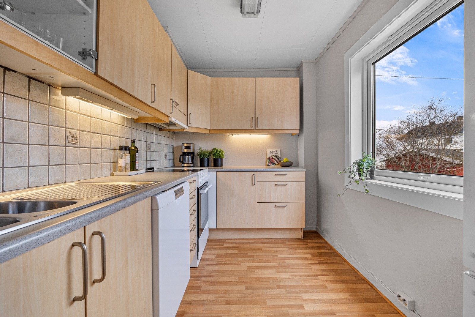Mellom benkeplate og overskap er det flislagt, som gjør rengjøringen enkel. Av hvitevarer er det komfyr, oppvaskmaskin samt kjøl-/fryseskap. Galleribilde