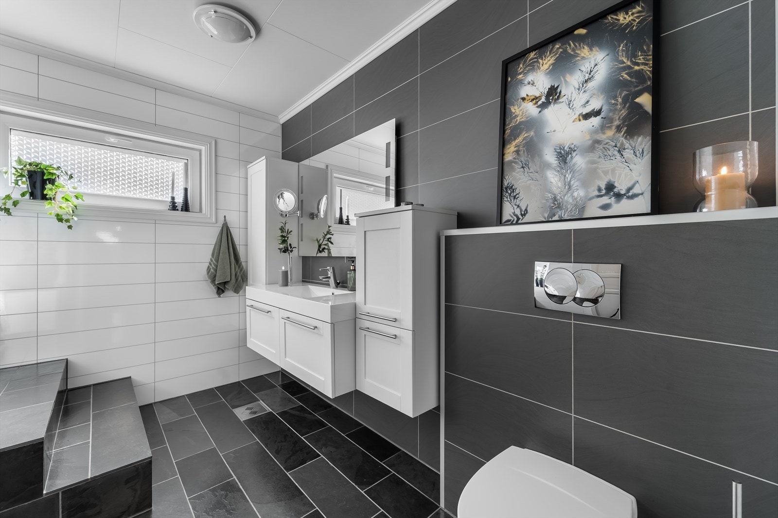 Delikat og moderne innredet bad med fliser på gulv og baderomsplater på vegg. Innredet med baderomsinnredning, toalett og innebygd badekar. Galleribilde