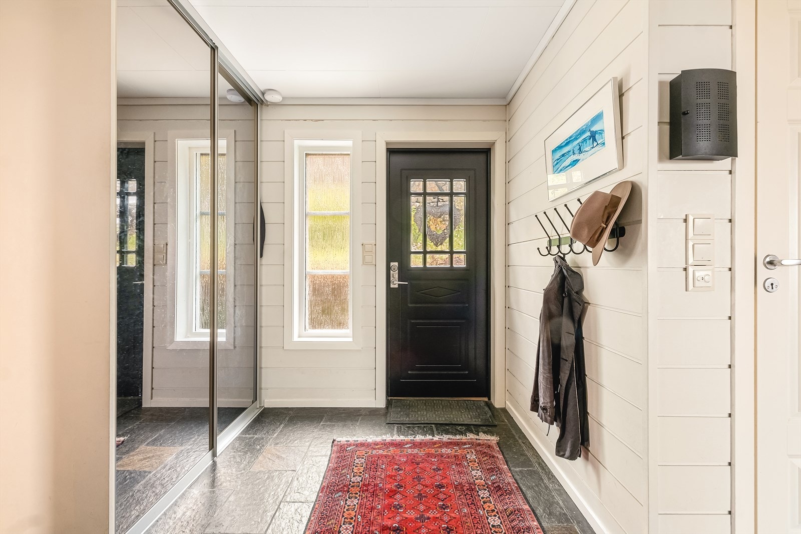 Velkommen inn! En romslig gang med skifer på gulv og romslig garderobeskap med speilfronter ønsker velkommen hjem. Galleribilde