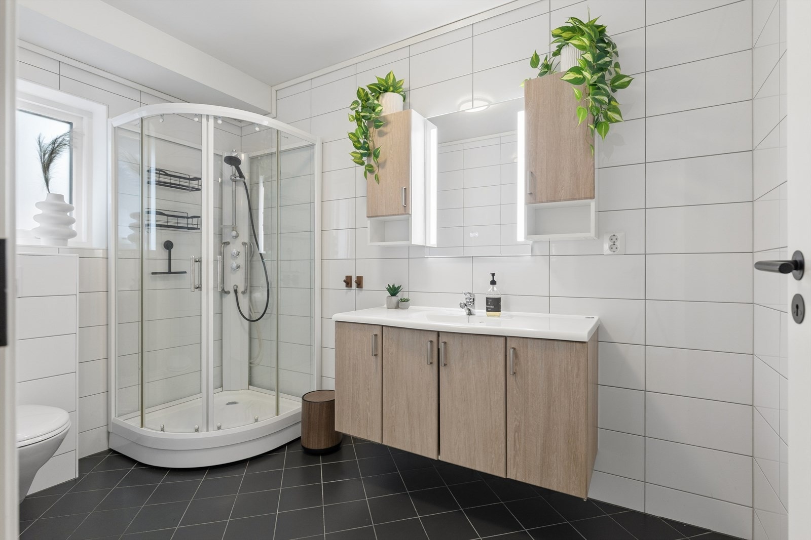 Badet har et tidløst uttrykk med keramiske fliser på gulv og vegger, og komforten sikres med varmekabler i gulvet. Rommet har avtrekk via det balanserte ventilasjonsanlegget. Galleribilde