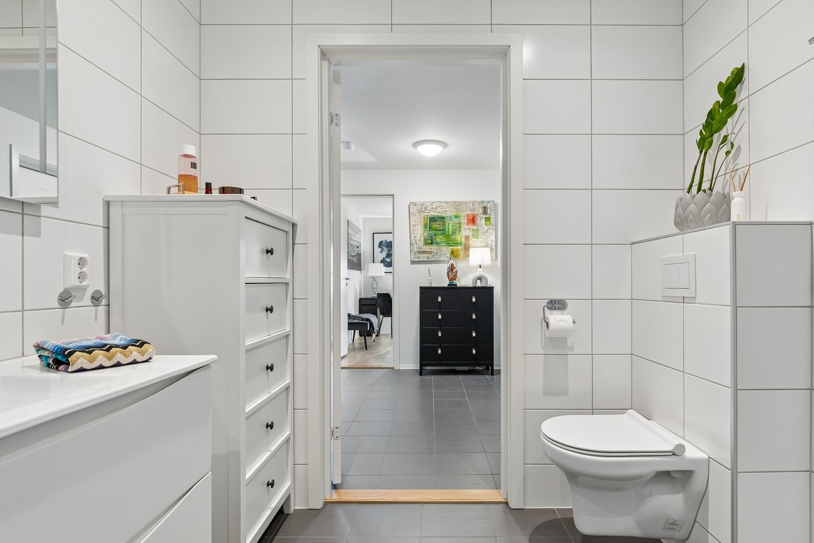 Innredningen har servant med hvite skuffer og speil med integrert belysning. Videre er toalettet vegghengt og dusjhjørnet har innfellbare glassdører. Galleribilde