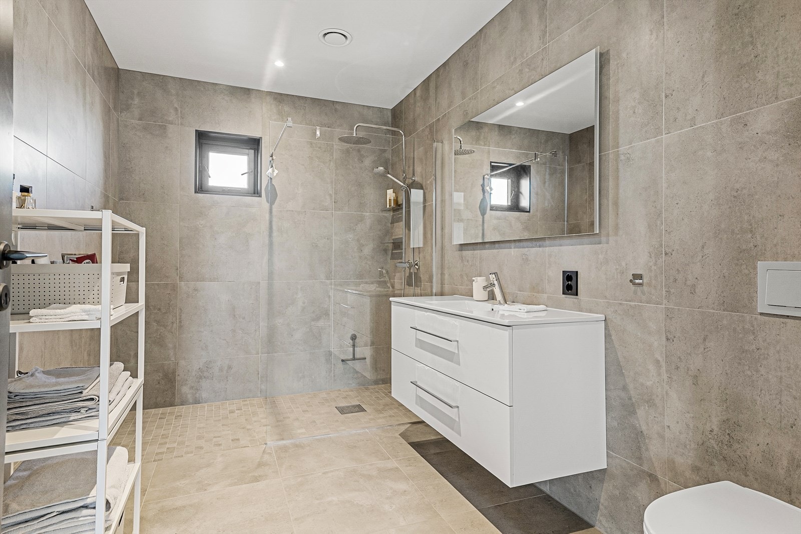 Badet er utstyrt med veggmontert toalett, innredning med nedfelt servant og dusjvegger/hjørne. Galleribilde