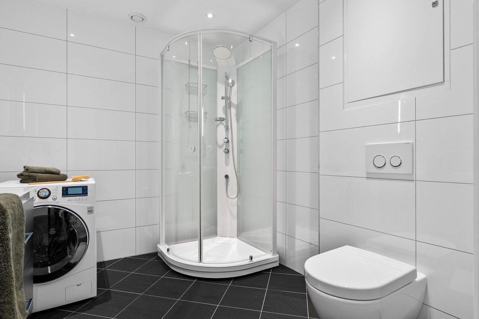 Badet er innredet med servant i møbel, vegghengt toalett, dusjkabinett og opplegg til vaskemaskin. Galleribilde