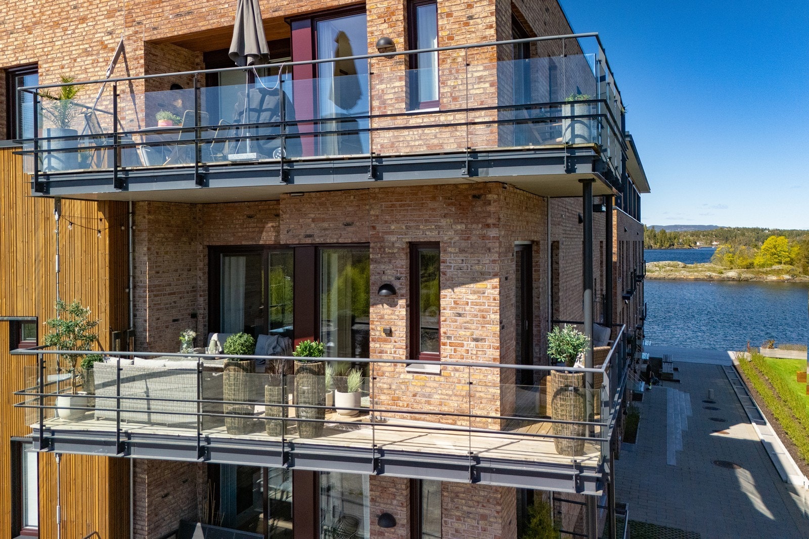 Balkongen strekker seg rundt hjørnet av bygget, med elegant glassrekkverk og tregulv. Galleribilde