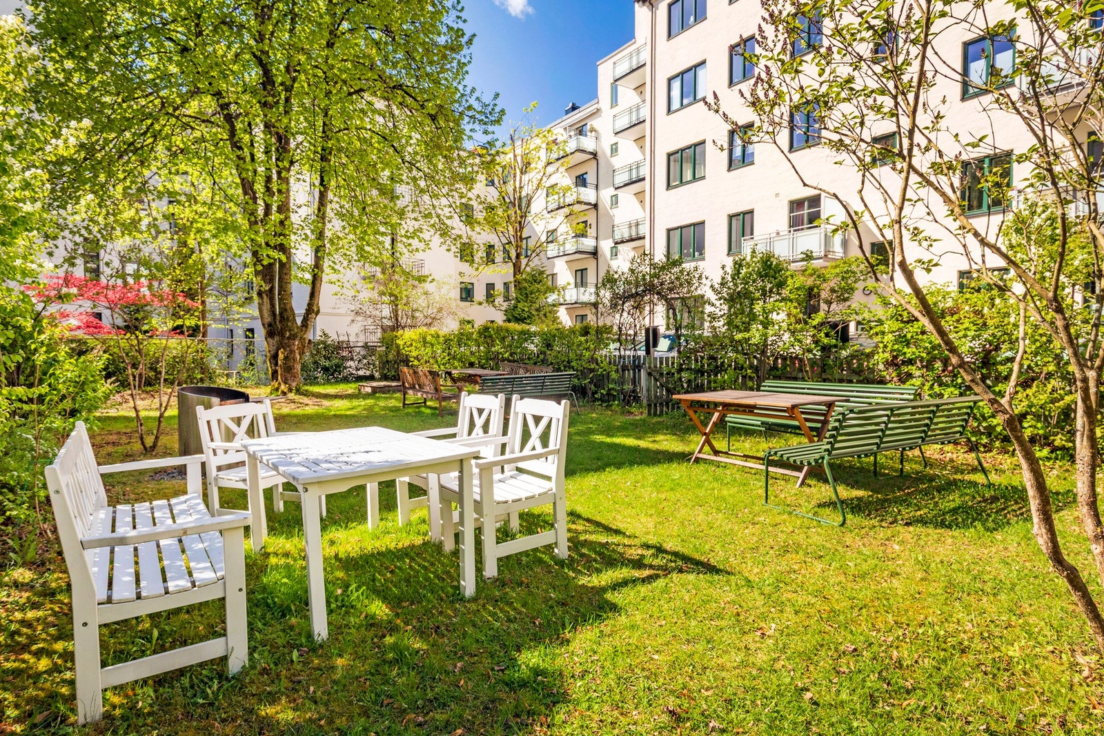 En koselig bakgård med sittegrupper og grill, omgitt av frodige, grønne trær som skaper en idyllisk sommerstemning. Galleribilde