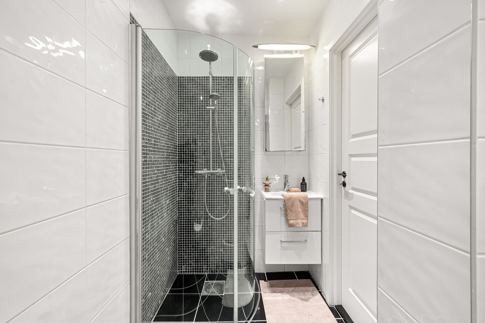 Badet inneholder baderomsmøbel med slette fronter, heldekkende servant, speilskap med belysning, vegghengt toalett og dusj med foldedører i herdet glass. Galleribilde
