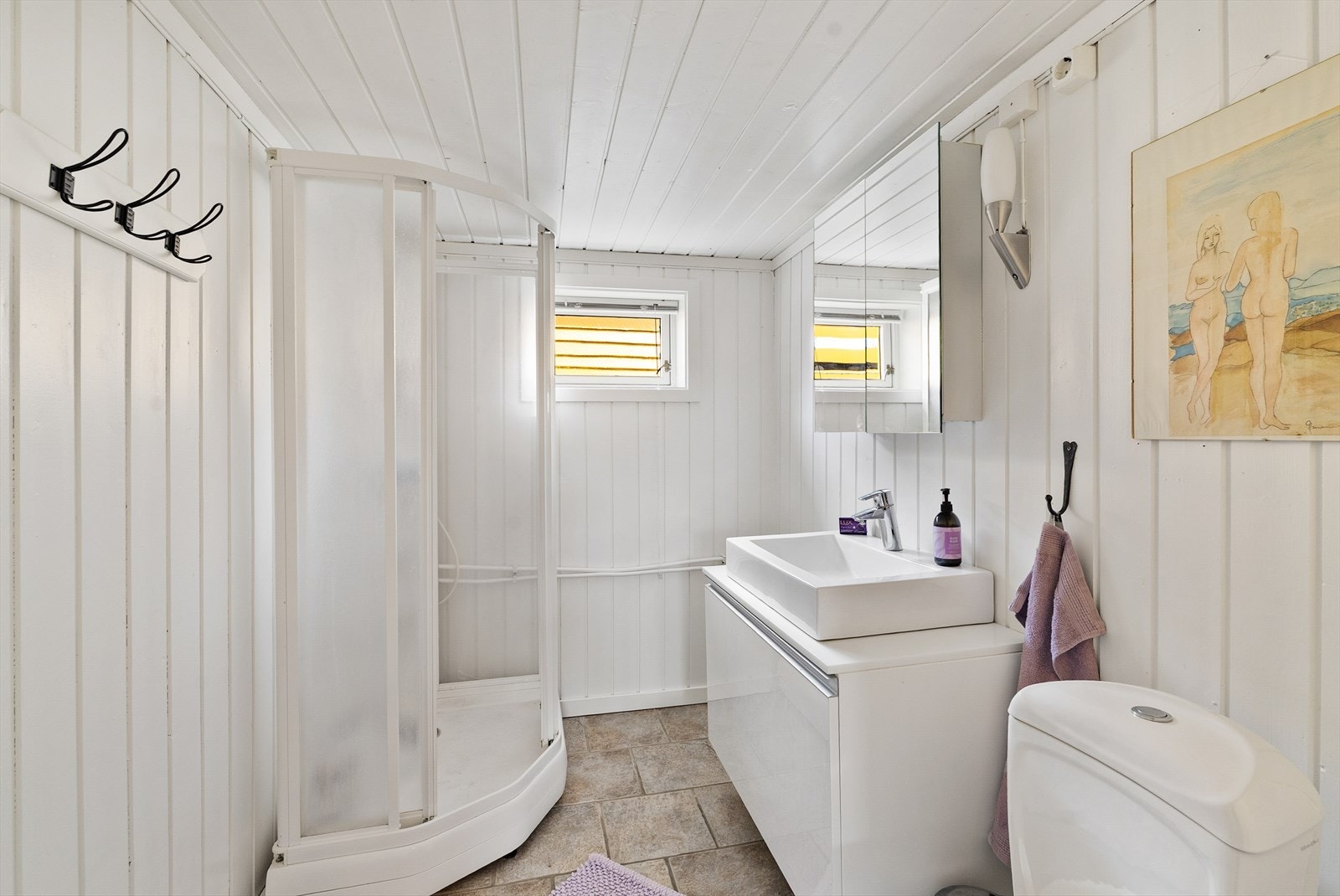 Badet i kjeller med flislagt gulv og panel på vegg. Varmekabler i gulvet. Rommet har innredning med nedfelt servant, speilskap, toalett og dusjkabinett. Galleribilde