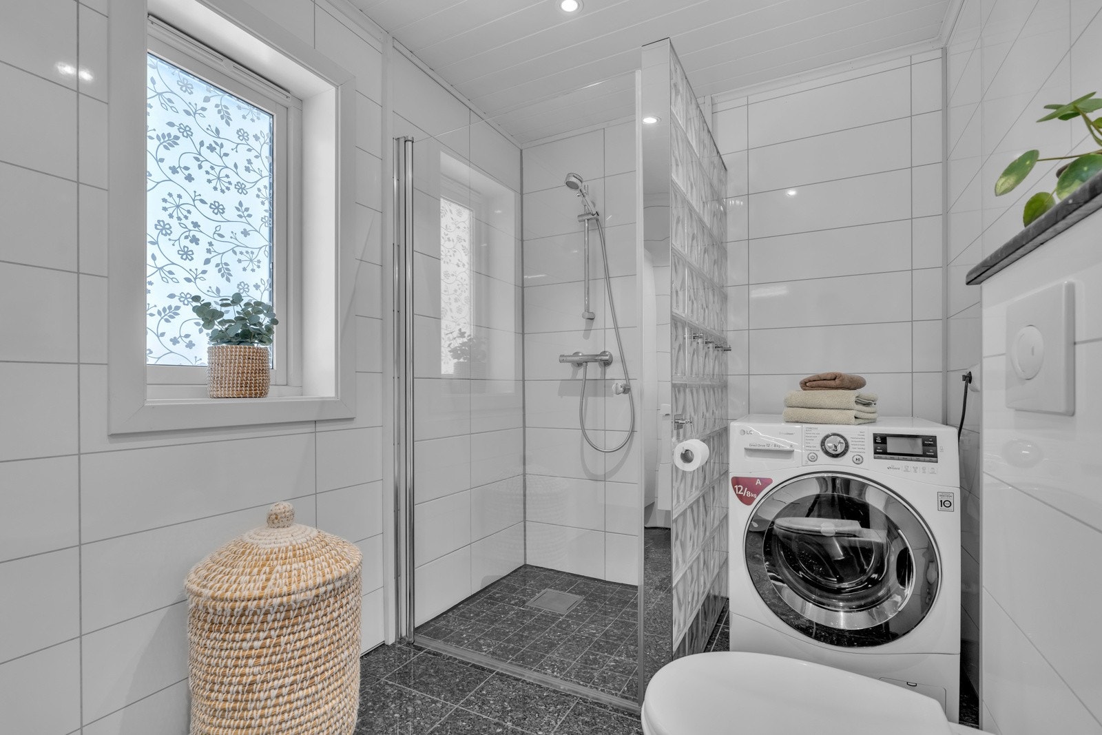 Badet har også dusjhjørne avskilt med glassbyggerstein og opplegg til vaskemaskin. Galleribilde