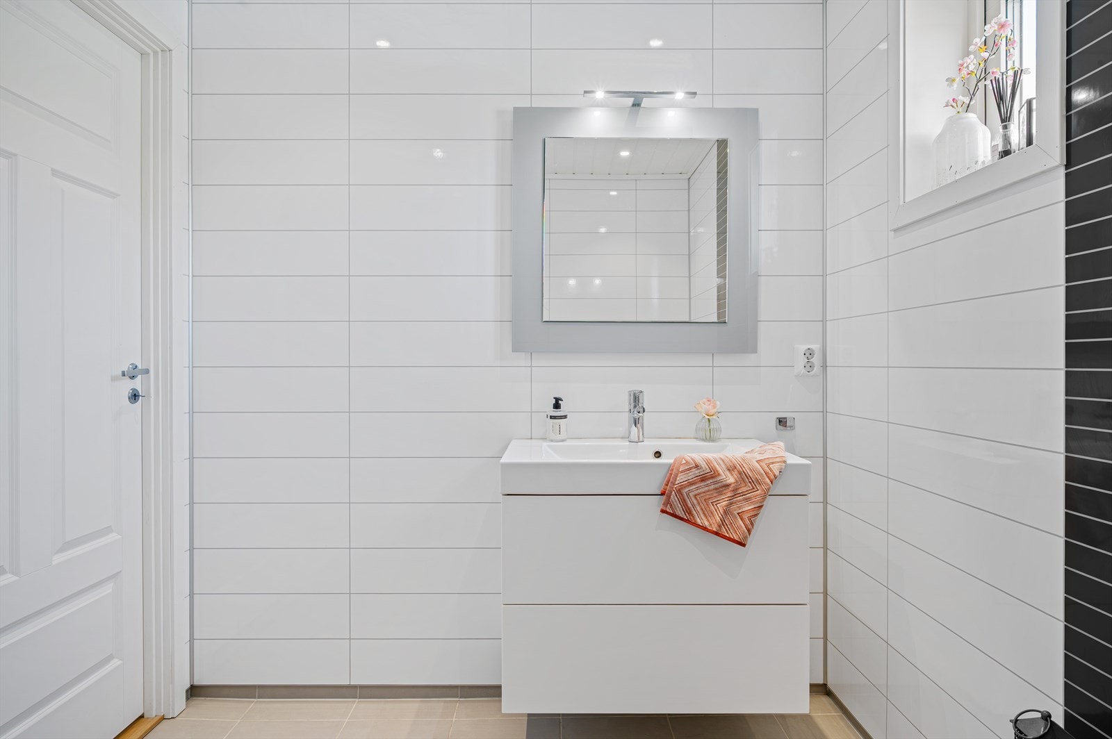 Badet inneholder baderomsmøbel med heldekkende servant, speil med belysning, vegghengt toalett og dusj med foldedører i herdet glass. Galleribilde