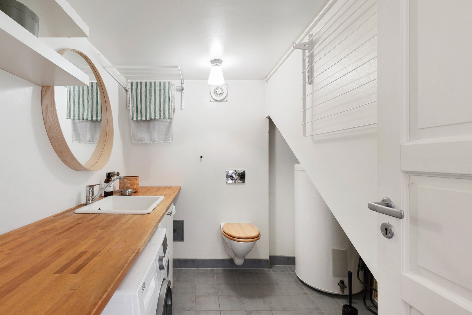 Praktisk vaskerom med opplegg for vaskemaskin, vegghengt toalett og stor benkeflate med servant. Galleribilde