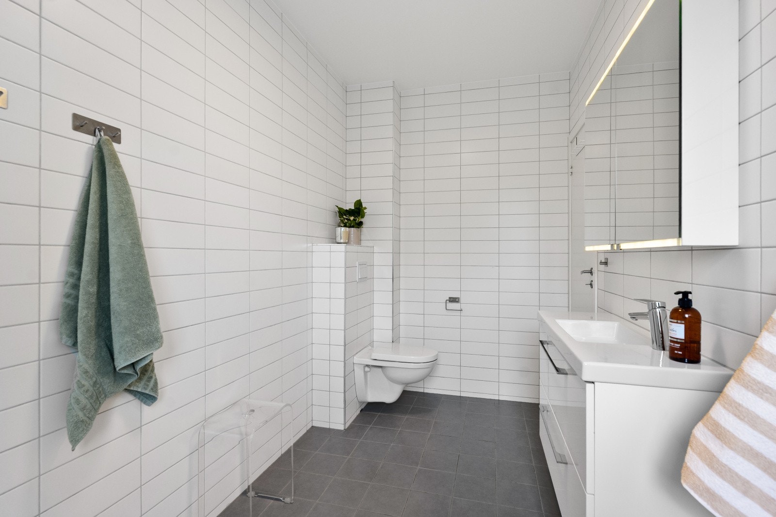 Badet har veggmontert toalett og flislagte vegger. Galleribilde