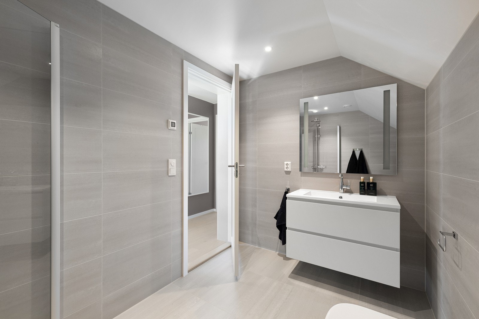 Badet fremstår som moderne og stilrent med flislagte vegger og gulv, samt malt himling som gir et lyst og tidløst uttrykk. Det er installert elektriske varmekabler i gulvet. Galleribilde