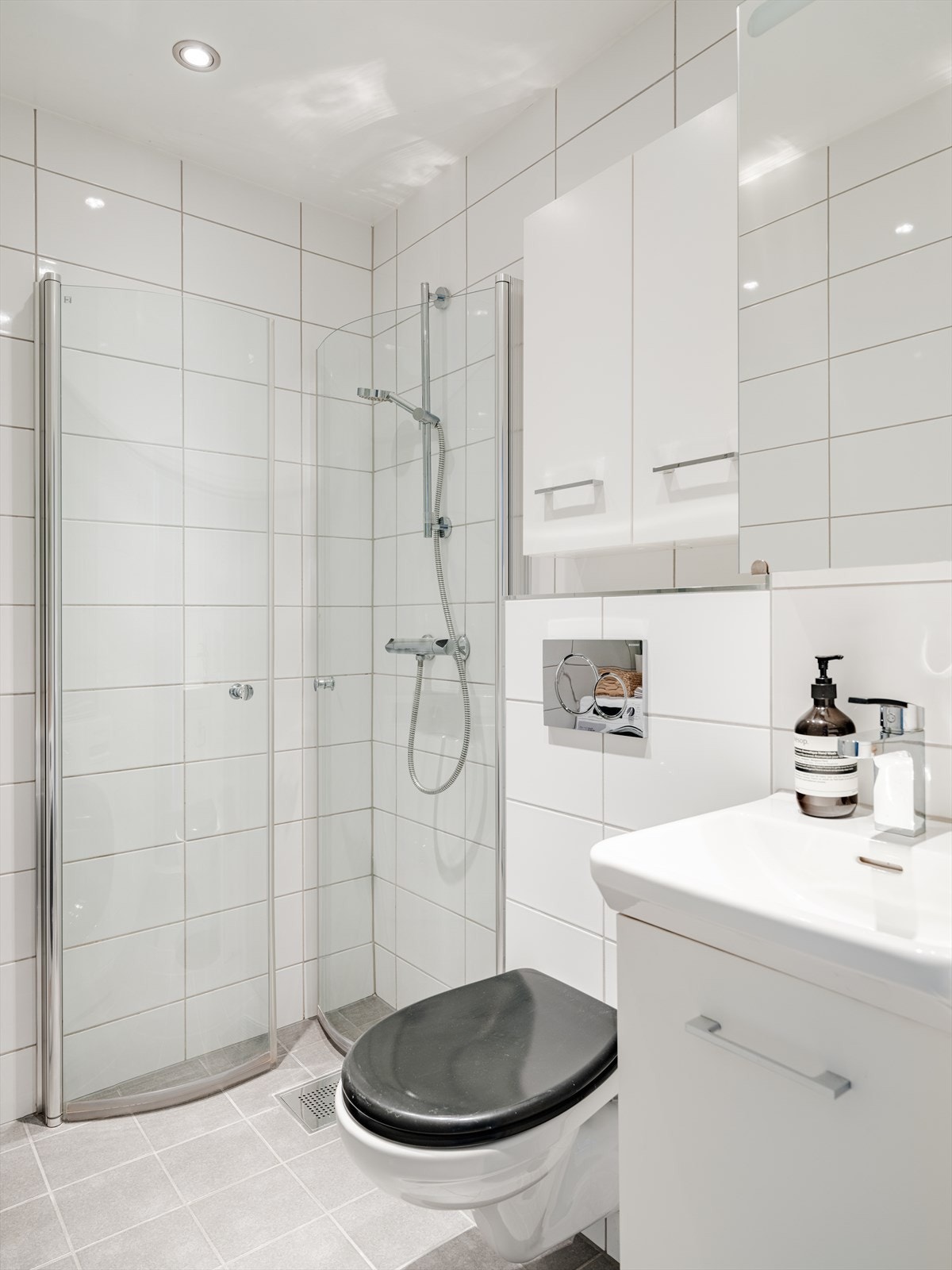 Badet inneholder veggmontert WC, dusjplass med inn-utadslående dusjvegger, servant og opplegg for vaskemaskin. Galleribilde