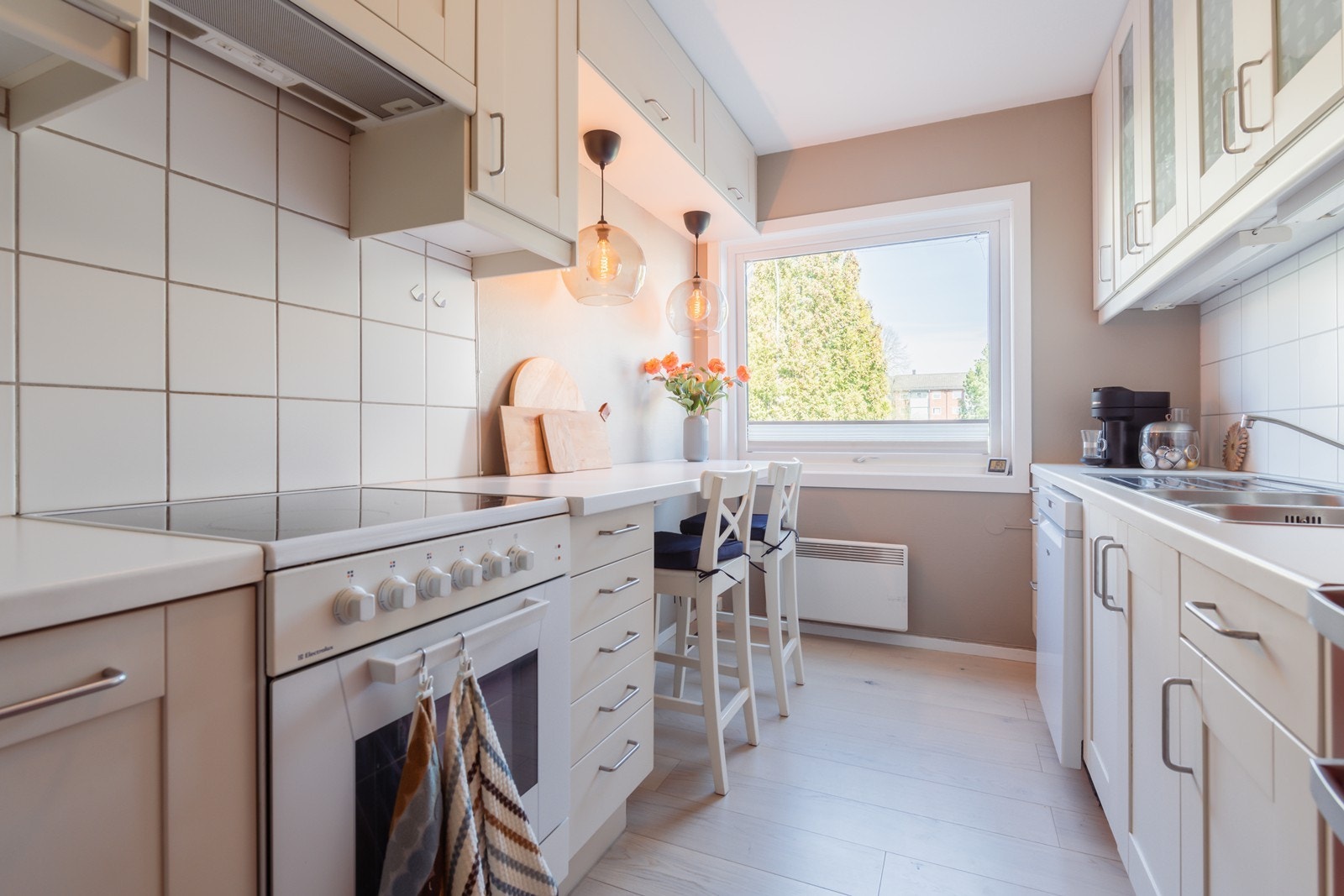 Kjøkkeninnredning med malte speilfronter, laminat benkeplate, stål oppvaskkum, mekanisk ventilator og frittstående hvitevarer. Galleribilde