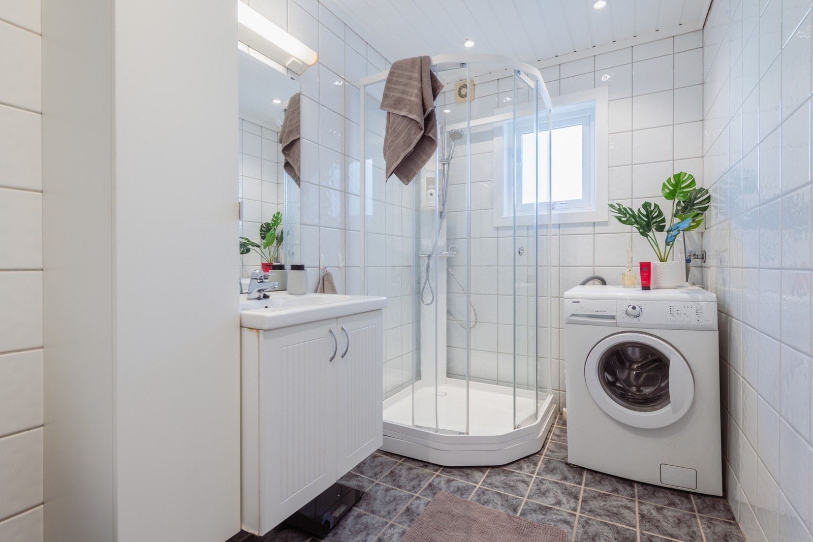 Bad med vaskeservant i innredning, gulvmontert wc og lukket dusjkabinett. Det er opplegg for vaskemaskin i rommet. Galleribilde