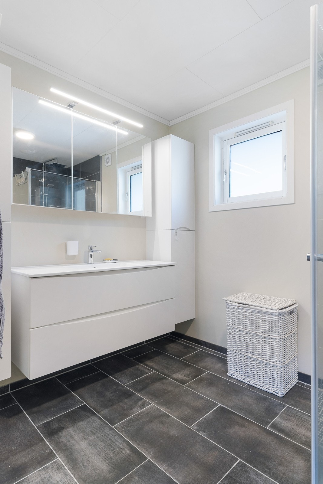 Romslig baderom med lyse vegger og mørke fliser på gulv. Stor innredning gir god oppbevaringsplass. Badet ble renovert i 2021. Galleribilde