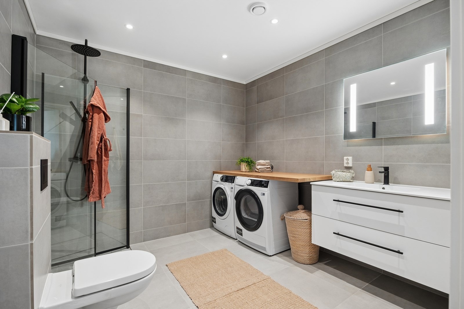 Badet måler 8,5 kvm og fremstår med lekre, store gulvfliser, gulvvarme og downlights i taket. Opplegg for vaskemaskin/tørketrommel. Galleribilde
