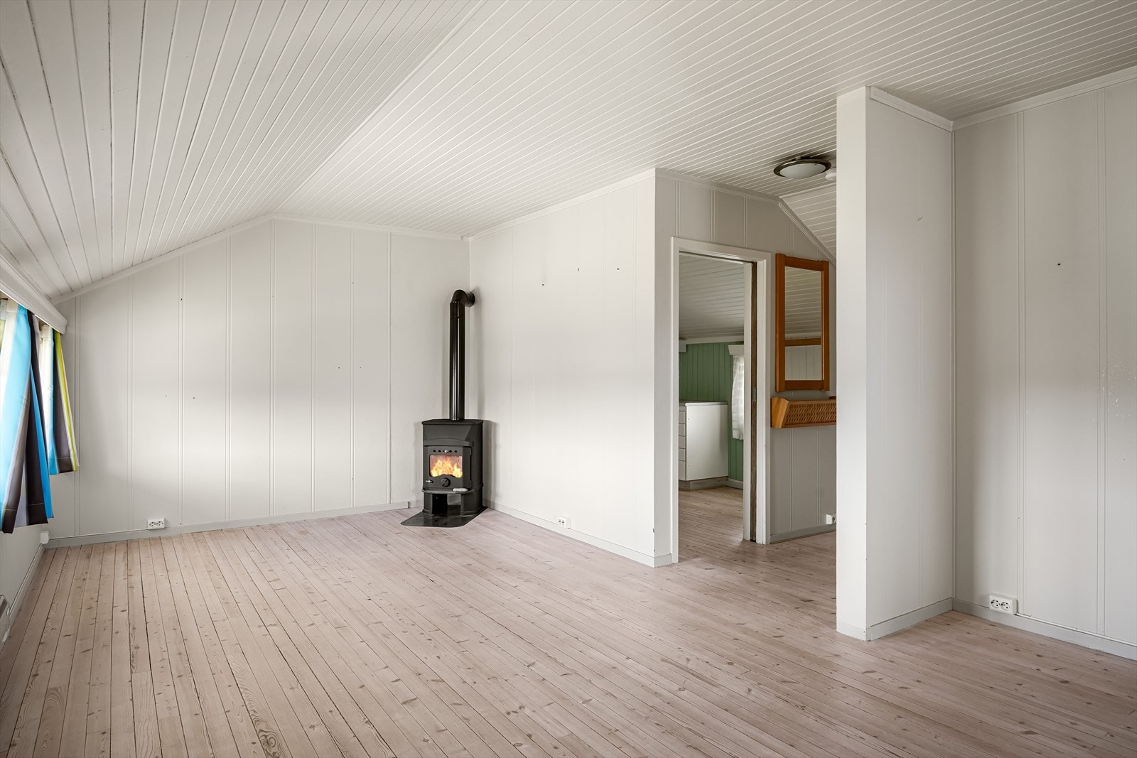 Lys og romslig stue i 2. etasje med tregulv og lysmalte overflater. I hjørnet er det en koselig peisovn som både gir god varme og bidrar til ekstra hygge. Galleribilde