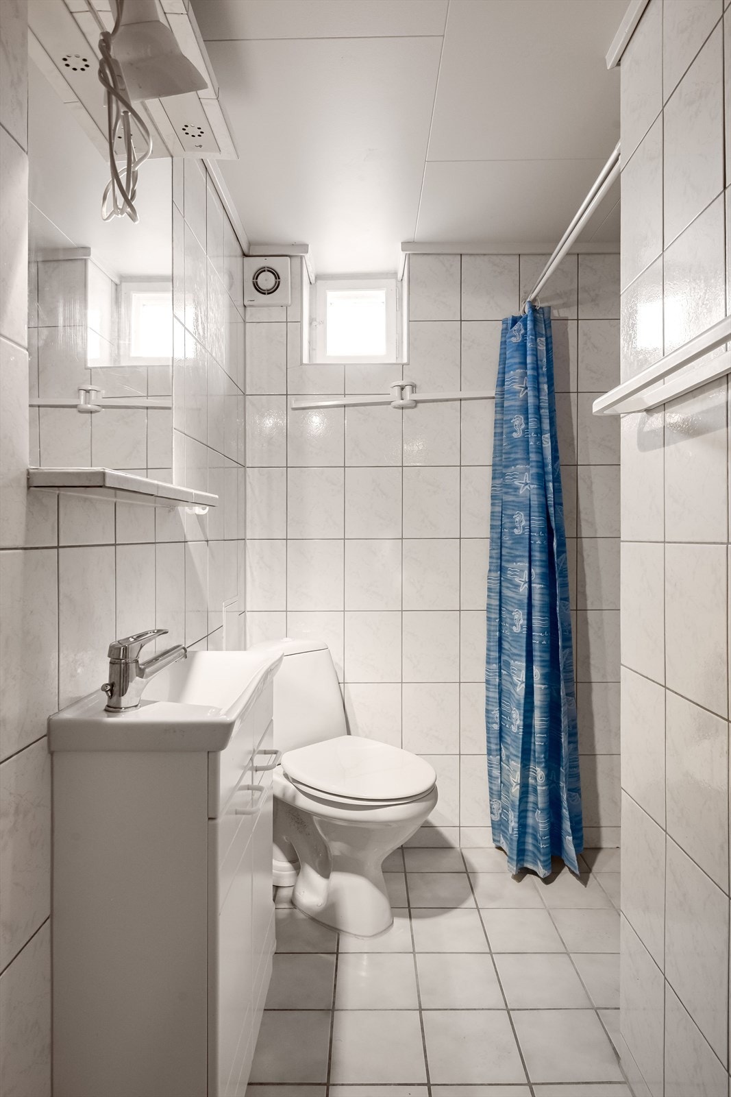 Baderom i kjeller med overflater, installasjoner og komponenter fra ca. 2005. Baderommet har fliser på gulv og vegger, gulvvarme og elektrisk styrt vifte. Galleribilde