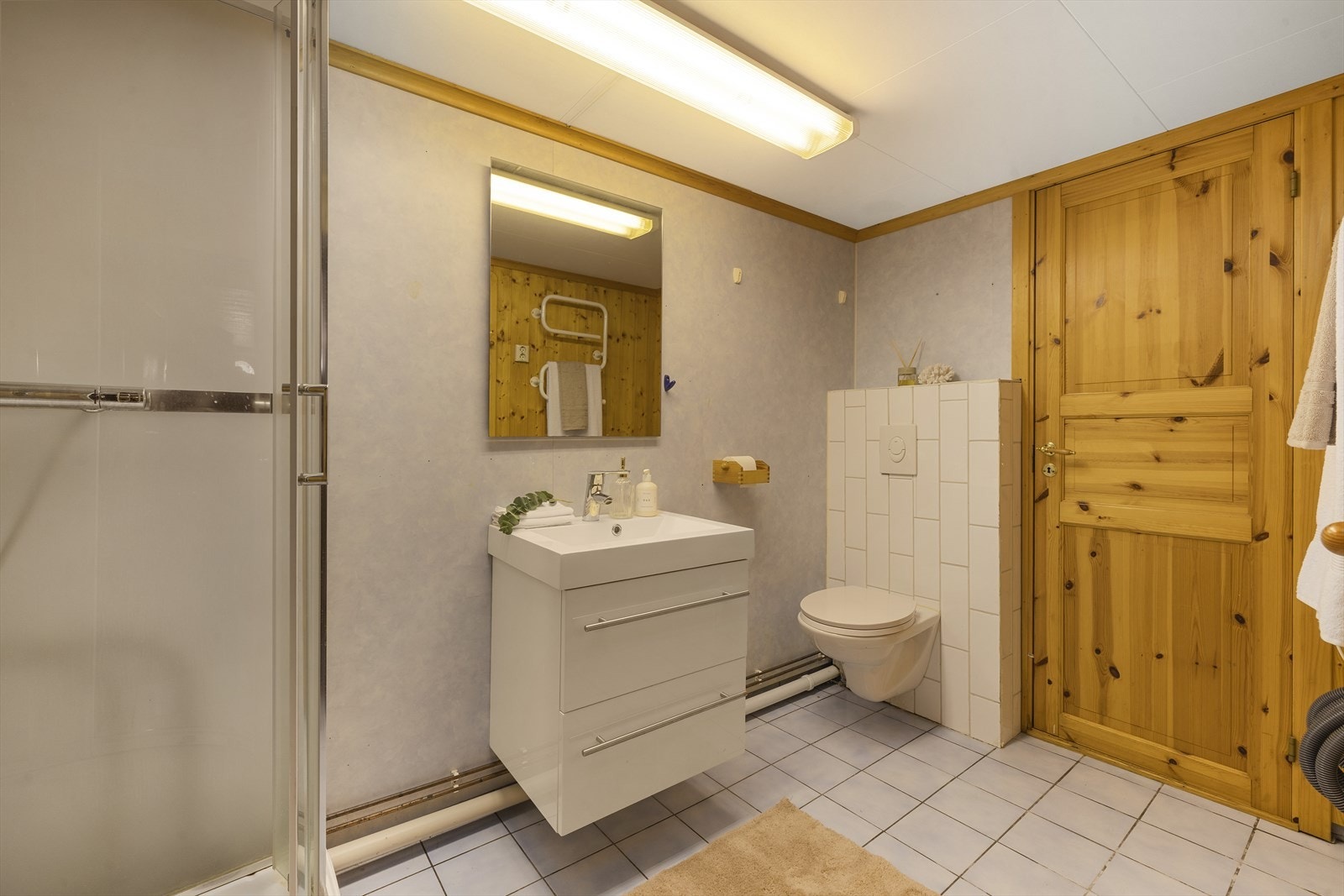 Badet er innredet med vegghengt toalett, servantinnredning og dusjkabinett. Flislagt gulv med varmekabler gir en lun og behagelig komfort. Galleribilde