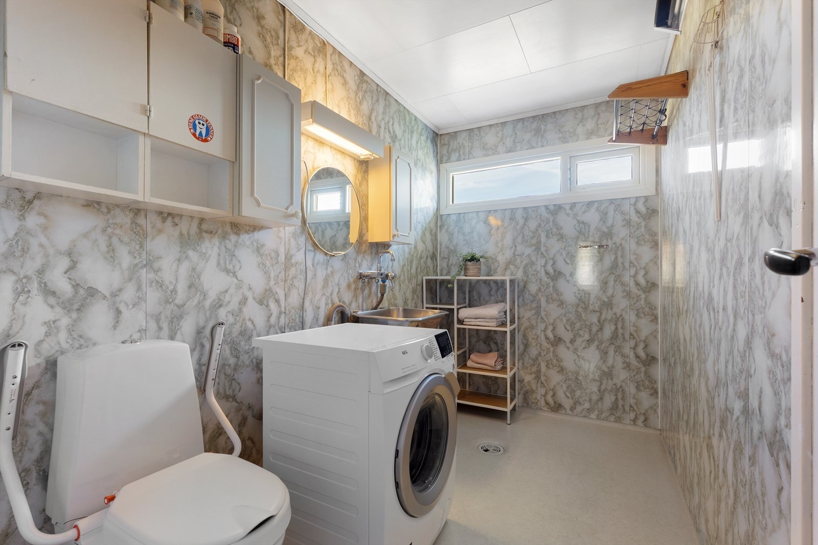 Separat vaskerom med vinylbelegg på gulv, opplegg for vaskemaskin og et gulvmontert toalett. Galleribilde