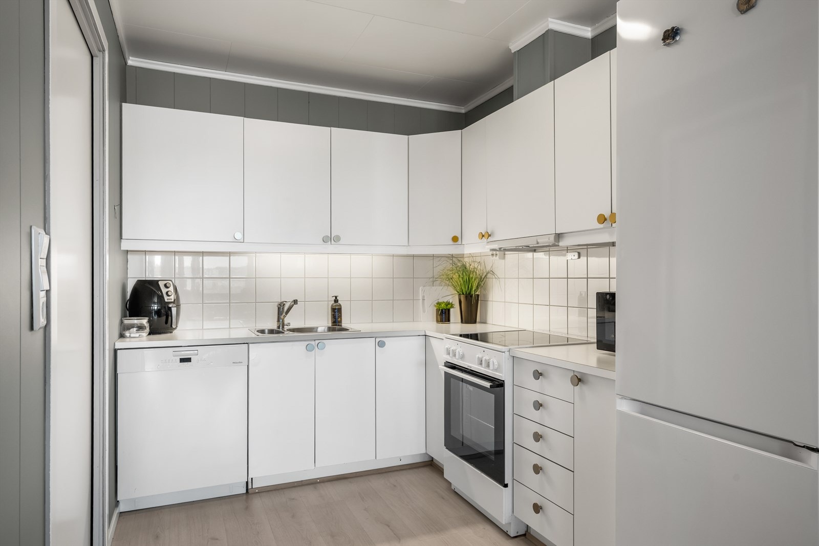 Kjøkkeninnredning med hvite, glatte fronter og laminatbenkeplate. Det er lagt fliser over benken. Galleribilde