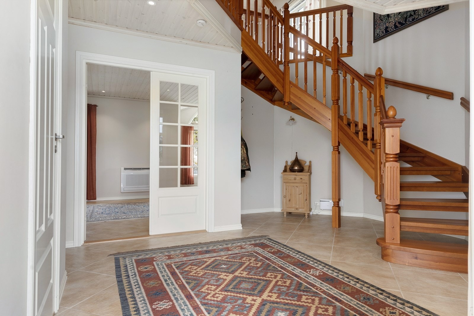 Entréen ønsker velkommen med flislagt gulv og vannbåren varme. Den massive tretrappen leder opp til andre etasje. Galleribilde