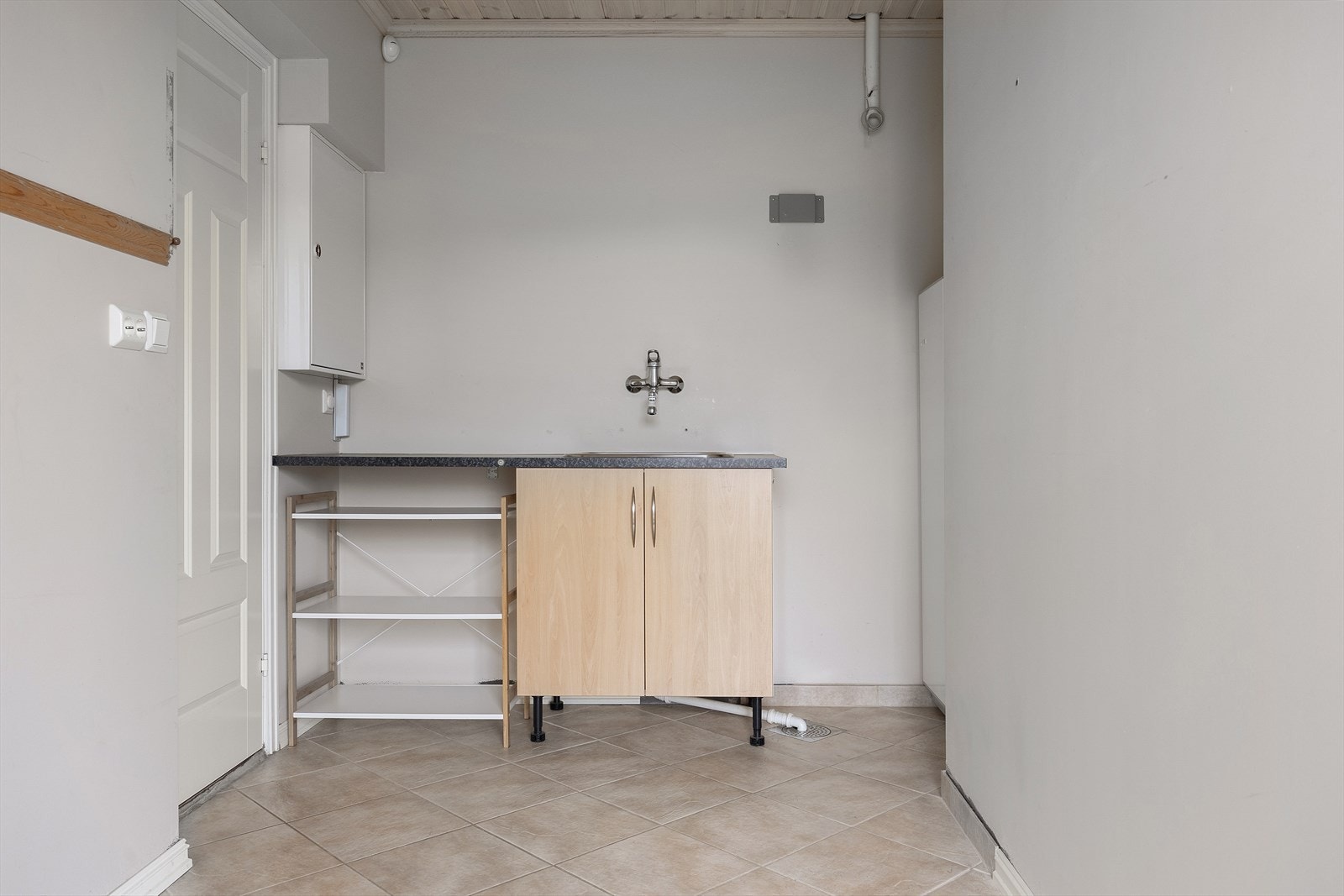Praktisk vaskerom med flislagt gulv, utslagsvask og opplegg for vaskemaskin. Her er også boligens tekniske installasjoner samlet. Galleribilde