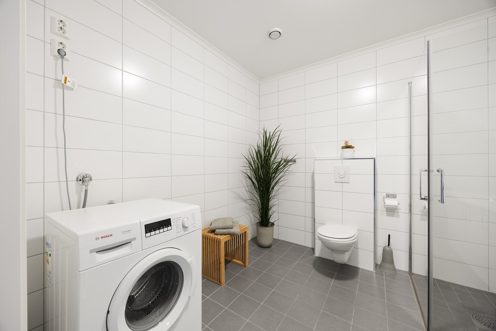 Badet er utstyrt med veggmontert toalett, dusjnisje med glassdører og opplegg for vaskemaskin. Galleribilde