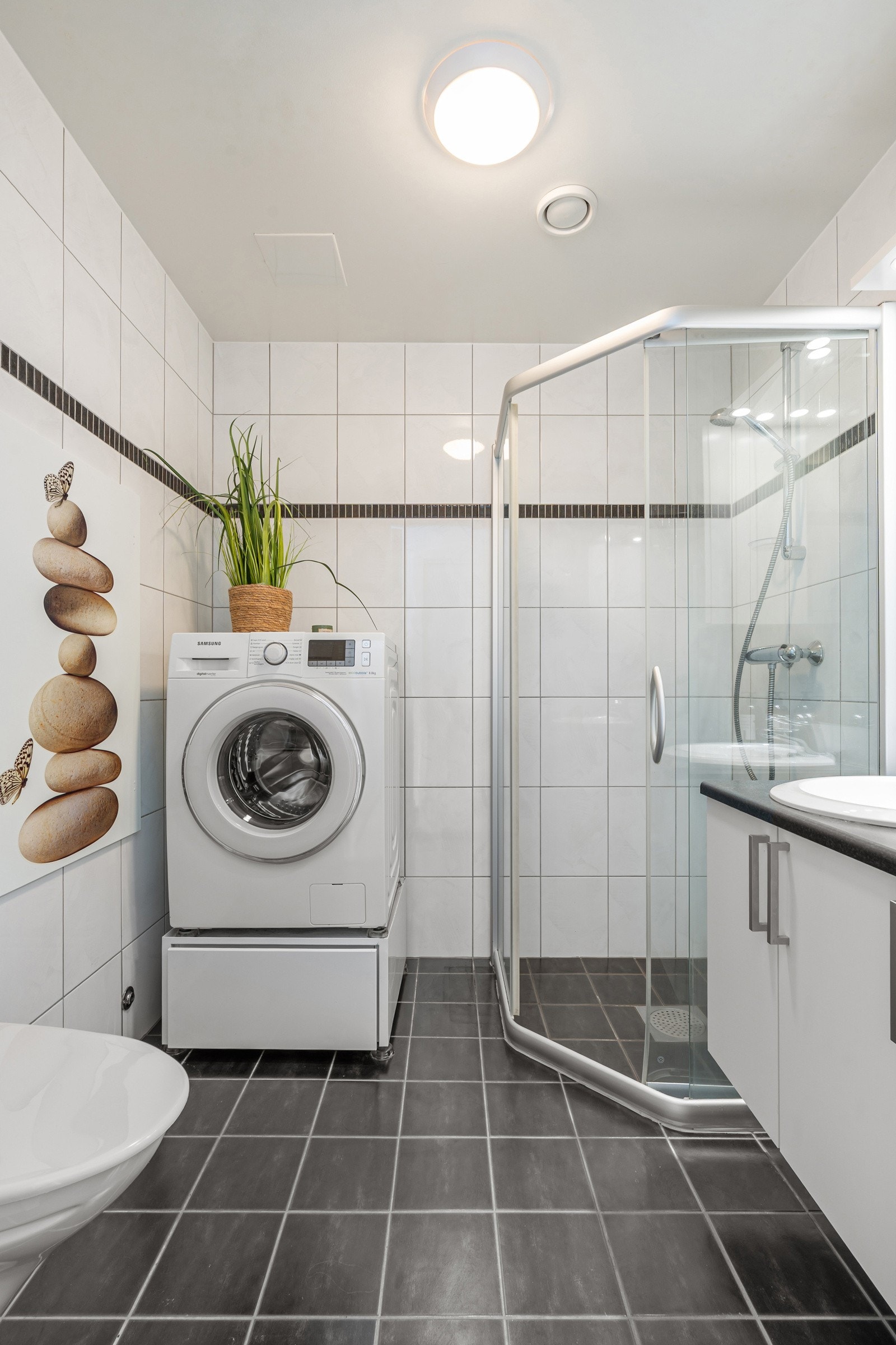 Pent og romslig bad med flislagte gulv- og veggflater, vannbåren gulvvarme, baderomsinnredning med god oppbevaringsplass og opplegg for vaskemaskin.