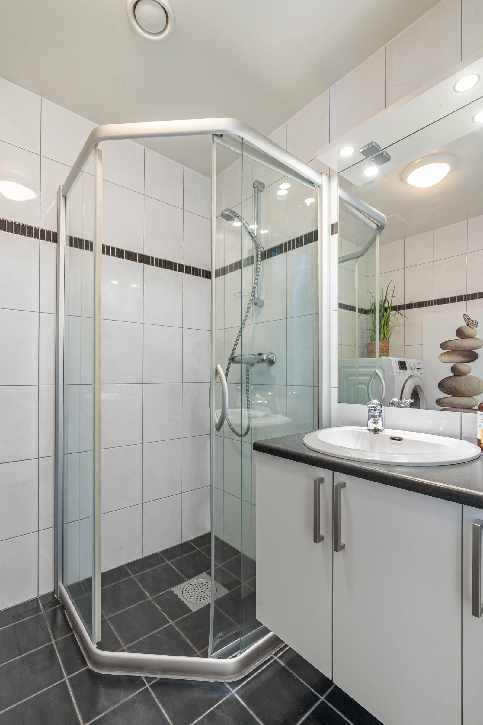 Badet er utstyrt med et stort dusjhjørne og et praktisk vegghengt toalett.