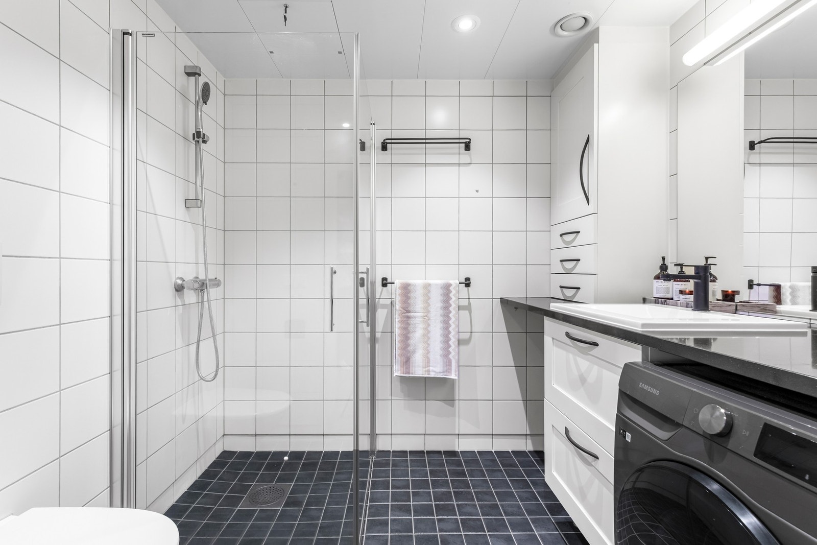 Badet har en romslig størrelse og inneholder opplegg for vaskemaskin, veggmontert toalett og dusjhjørne med svingdører. Galleribilde