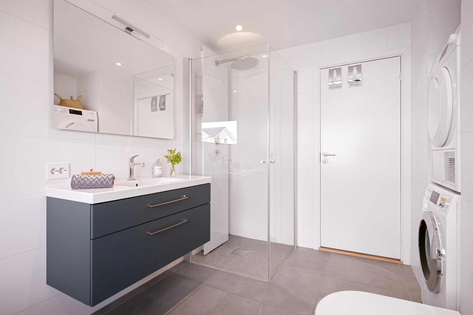 Badet er innredet med vegghengt toalett, dusj med glassvegger, badekar og moderne baderomsinnredning med servant og speil. Galleribilde