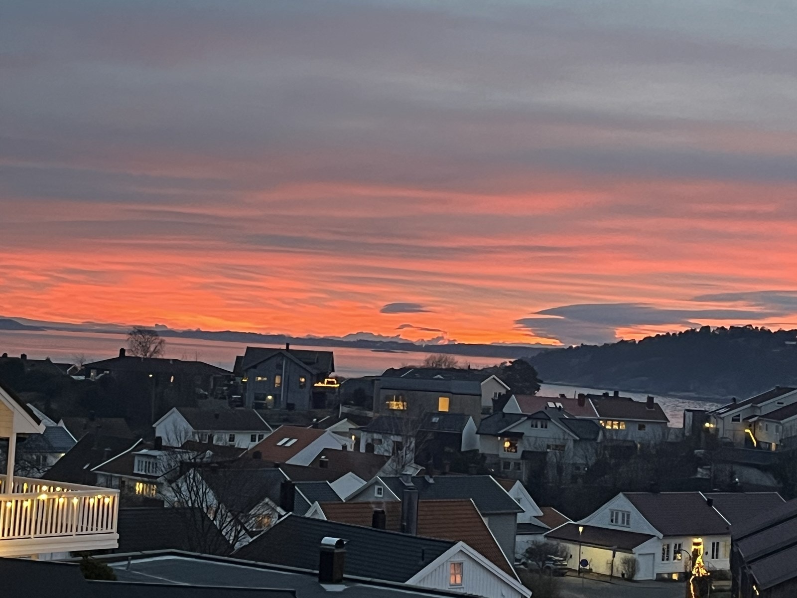 Hus og nabolag med utsikt mot vann og kystområde ved solnedgang. Galleribilde